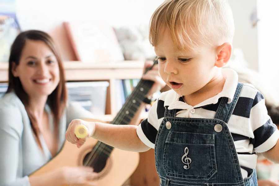 Un très jeune enfant lors d'une séance d'éveil musical avec l'animatrice de la session et sa guitare en second plan