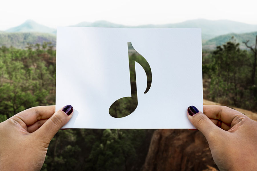 Une main tient une carte avec une note de musique découpée, sur un fond naturel, avec une illustration musicale blanche en surimpression