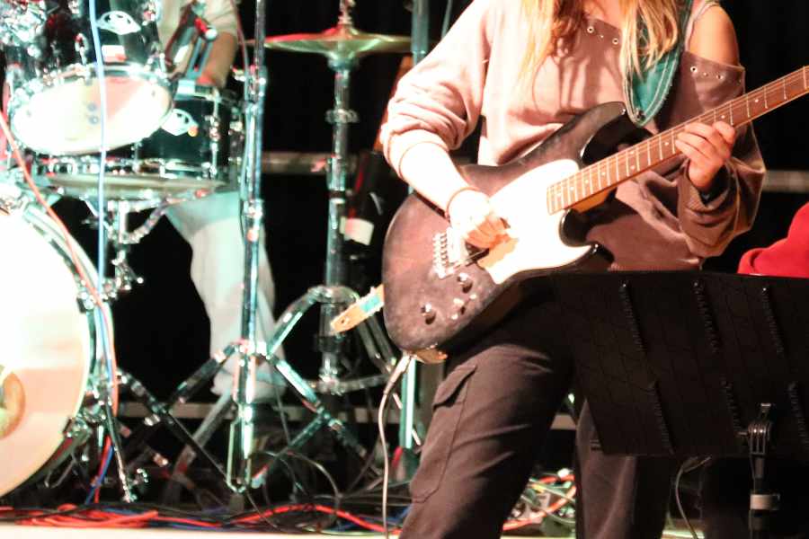 Élève jouant de la guitare électrique sur scène, accompagnée d’une batterie, lors d’un ensemble pop rock.